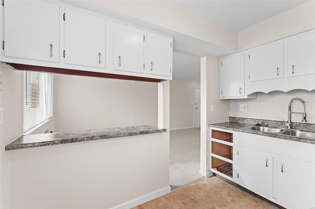 kitchen with a sink, tasteful backsplash, white cabinetry, and baseboards
