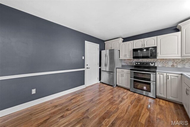 2915 Coram Dr, Saint Louis, MO 63129 - kitchen featuring appliances with stainless steel finishes, decorative backsplash, wood finished floors, white cabinets, and baseboards