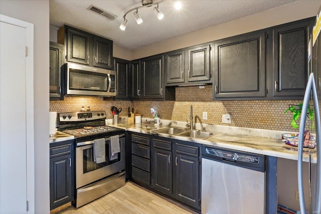 kitchen with appliances with stainless steel finishes, a sink, light countertops, tasteful backsplash, and a textured ceiling