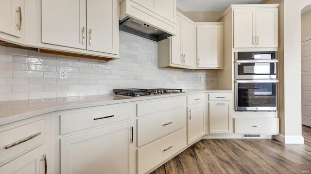 149 Haven Ridge Ct, Dardenne Prairie, MO 63368 - kitchen with premium range hood, double oven, dark wood finished floors, white cabinets, and tasteful backsplash