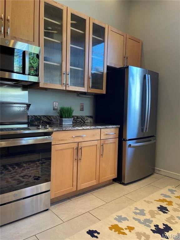 1906 Lasalle St, Saint Louis, MO 63104 - kitchen featuring appliances with stainless steel finishes, light tile patterned floors, glass insert cabinets, dark stone countertops, and baseboards