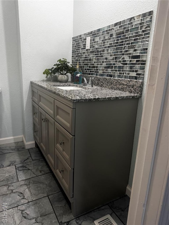 bathroom featuring marble finish flooring, backsplash, vanity, and baseboards