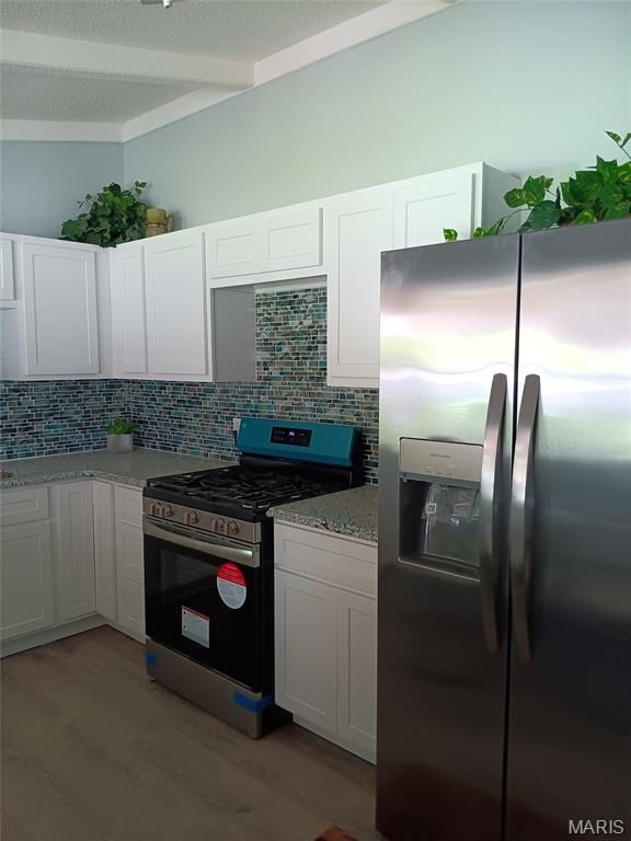 kitchen featuring appliances with stainless steel finishes, decorative backsplash, light wood-style flooring, white cabinetry, and beamed ceiling