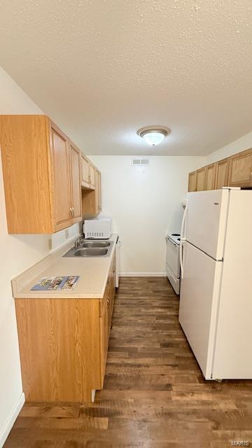 kitchen featuring white appliances, a sink, dark wood-style floors, a textured ceiling, and baseboards