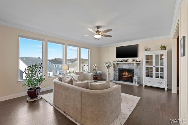 living room featuring a stone fireplace, a ceiling fan, ornamental molding, dark wood-style floors, and baseboards