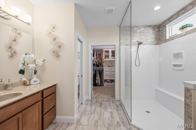 bathroom featuring walk in shower, a spacious closet, wood finished floors, vanity, and baseboards