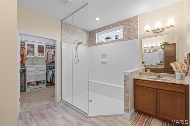 full bathroom featuring walk in shower, vanity, a spacious closet, and wood finished floors