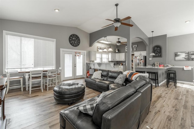 living room featuring ceiling fan, arched walkways, light wood finished floors, high vaulted ceiling, and baseboards