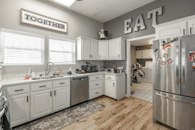 kitchen with stainless steel appliances, a sink, washer / clothes dryer, and white cabinets