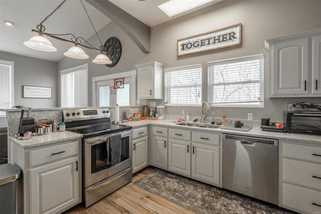 kitchen with appliances with stainless steel finishes, a sink, a peninsula, light wood-style floors, and white cabinets