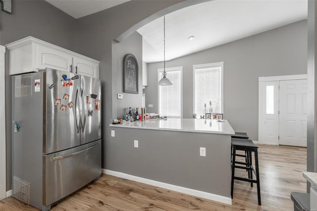 kitchen with freestanding refrigerator, arched walkways, a peninsula, white cabinets, and a kitchen bar