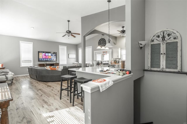 kitchen with ceiling fan, light wood finished floors, white cabinetry, arched walkways, and a kitchen breakfast bar