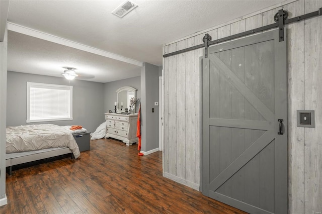 bedroom with a barn door, wood finished floors, baseboards, and wooden walls