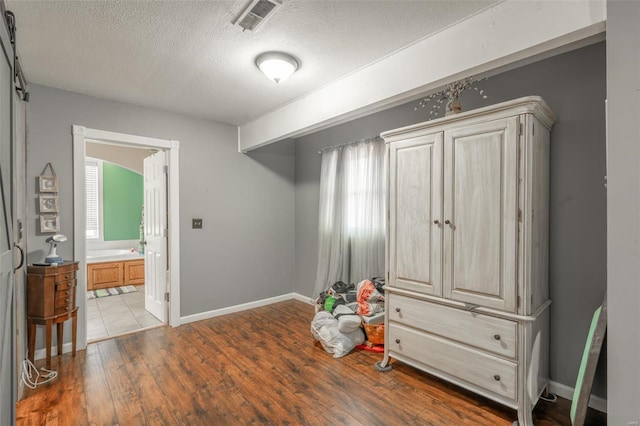 bedroom featuring a textured ceiling, wood finished floors, ensuite bathroom, and baseboards