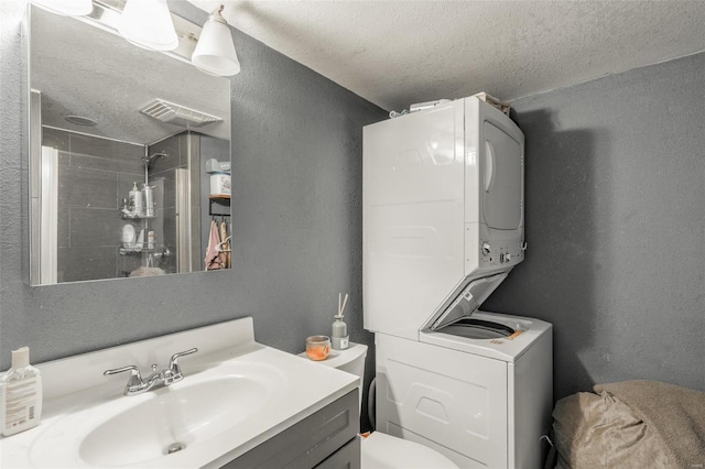 full bathroom featuring tiled shower, a textured ceiling, vanity, a textured wall, and toilet