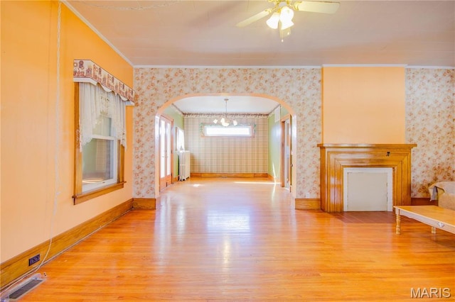 708 E Fillmore St E, Fillmore, IL 62032 - unfurnished living room featuring radiator heating unit, wallpapered walls, arched walkways, wood finished floors, and ornamental molding