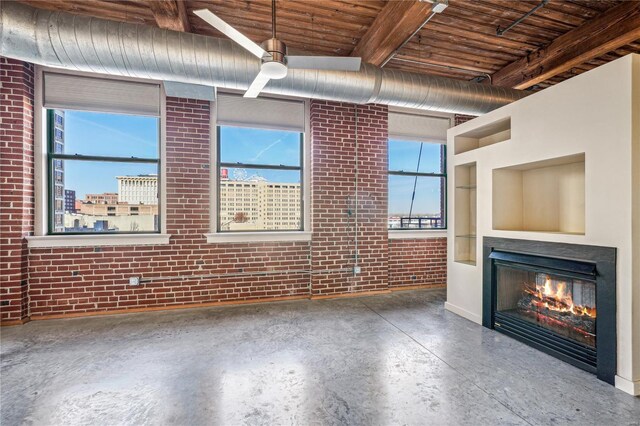 unfurnished living room with wood ceiling, a lit fireplace, concrete floors, brick wall, and a ceiling fan