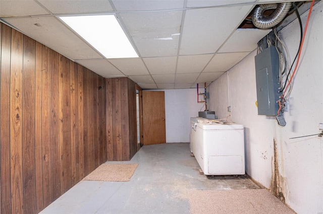 finished below grade area featuring wood walls, electric panel, a drop ceiling, and washer / clothes dryer