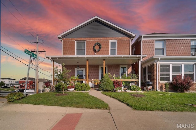 view of front of home featuring brick siding, covered porch, and a lawn