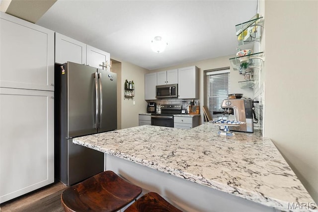 kitchen with appliances with stainless steel finishes, a peninsula, dark wood finished floors, light stone counters, and decorative backsplash