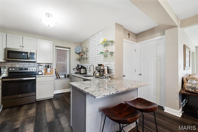 kitchen featuring stainless steel appliances, a sink, a breakfast bar area, and dark wood-style floors