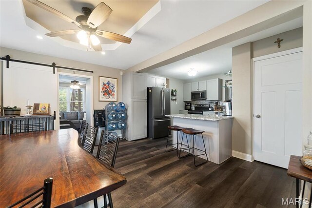 dining area with ceiling fan, dark wood-type flooring, a barn door, recessed lighting, and baseboards