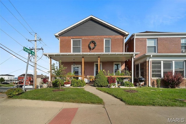 view of front of home with brick siding, a front yard, and covered porch