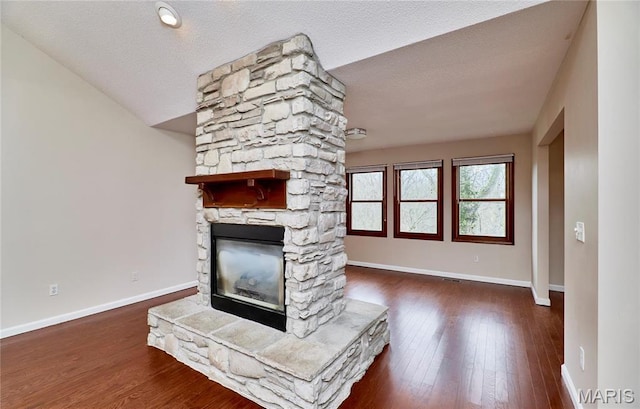 unfurnished living room with baseboards, a stone fireplace, and wood finished floors