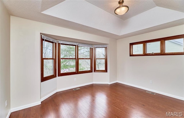 spare room with wood finished floors, baseboards, a textured ceiling, and a tray ceiling