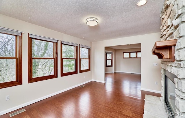 unfurnished living room with wood finished floors, a fireplace, a textured ceiling, and baseboards