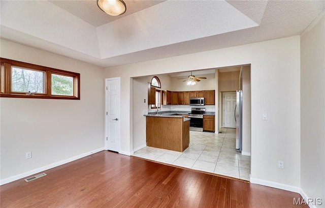 kitchen featuring appliances with stainless steel finishes, brown cabinetry, a peninsula, light wood-type flooring, and baseboards