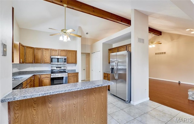 kitchen with appliances with stainless steel finishes, ceiling fan, brown cabinets, light tile patterned flooring, and beamed ceiling