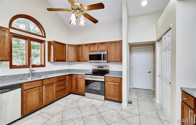 kitchen with appliances with stainless steel finishes, a sink, high vaulted ceiling, brown cabinets, and a ceiling fan