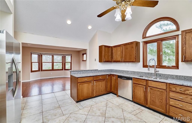 kitchen with stainless steel appliances, a sink, brown cabinets, a ceiling fan, and high vaulted ceiling