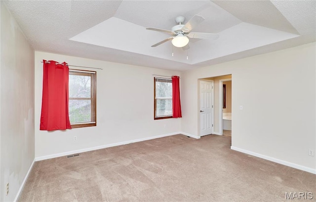 empty room with carpet flooring, ceiling fan, baseboards, and a raised ceiling