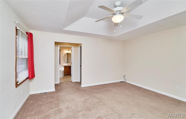 empty room with carpet flooring, ceiling fan, baseboards, a tray ceiling, and a textured ceiling