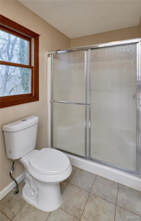 bathroom with tile patterned floors, a shower with door, toilet, and baseboards