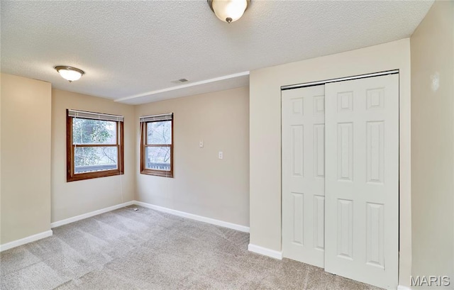 unfurnished bedroom with light colored carpet, a textured ceiling, baseboards, and a closet