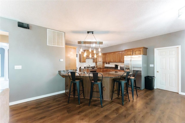 kitchen featuring stainless steel fridge, a peninsula, a breakfast bar area, dark wood-type flooring, and baseboards