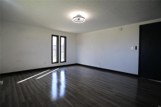 empty room featuring dark wood-style flooring, baseboards, and a textured ceiling