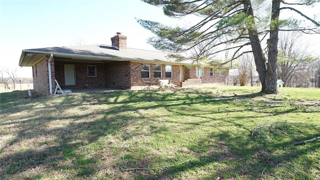 back of house featuring a chimney, brick siding, a lawn, and a patio area