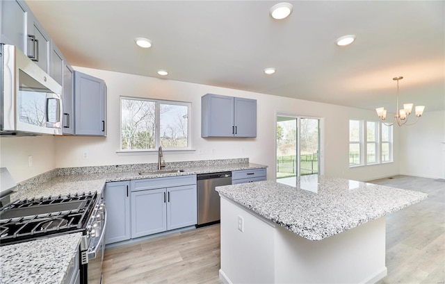 kitchen with stainless steel appliances, a sink, a chandelier, light stone counters, and light wood-style flooring