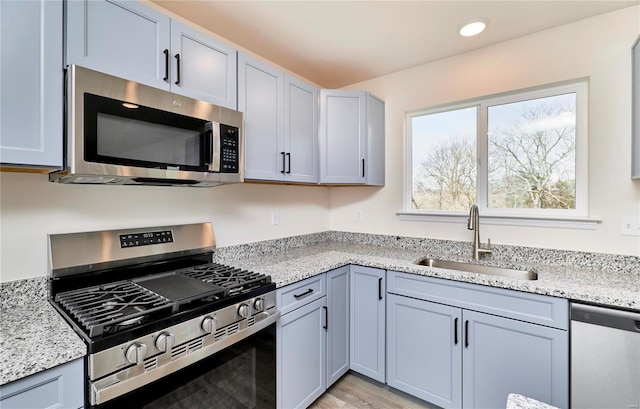 kitchen with stainless steel appliances, a sink, light stone counters, light wood finished floors, and recessed lighting