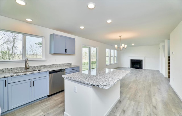 kitchen with a sink, stainless steel dishwasher, a chandelier, light wood-style flooring, and light stone counters