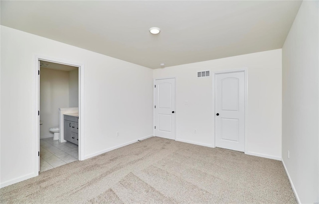 unfurnished bedroom featuring light colored carpet, baseboards, and ensuite bath