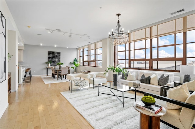living area with a chandelier, track lighting, baseboards, and light wood-style flooring