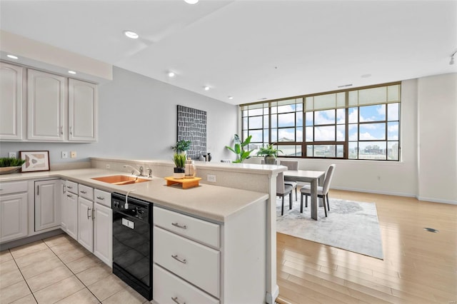 kitchen with dishwasher, a peninsula, a sink, light countertops, and white cabinets