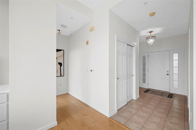 entryway featuring a chandelier, baseboards, and light wood-type flooring