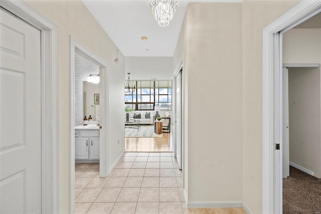 corridor featuring a chandelier, light tile patterned flooring, and baseboards