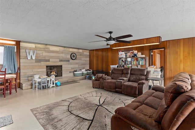 living room featuring wood walls, a ceiling fan, and a fireplace